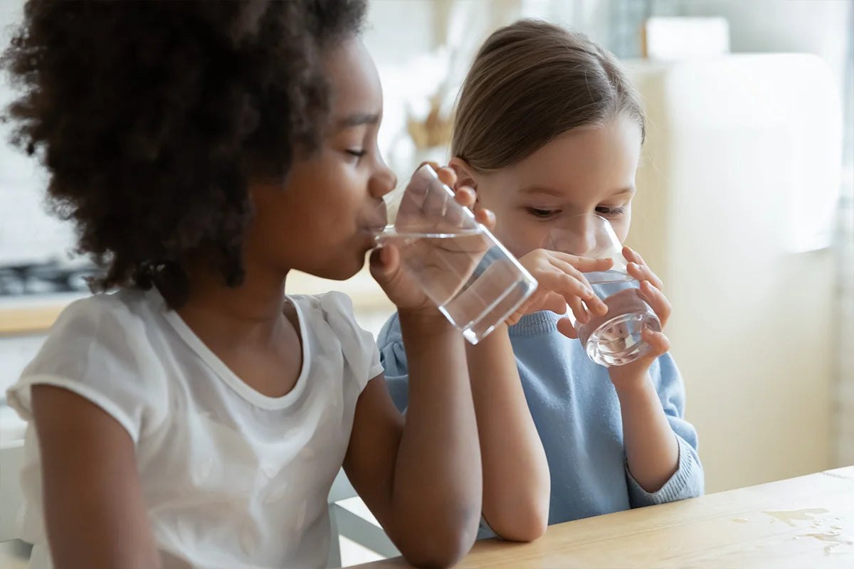 Little Black and little caucasian girl drinking from water glasses together.