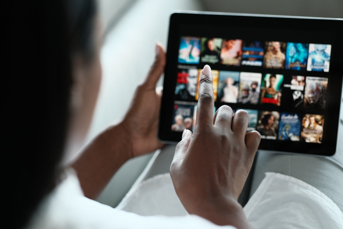 Young Black woman looking at the new documentaries on Netflix on her tablet. 