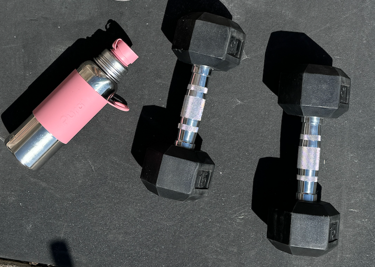Stainless steel sports water bottle next to a set of heavy black dumbells.