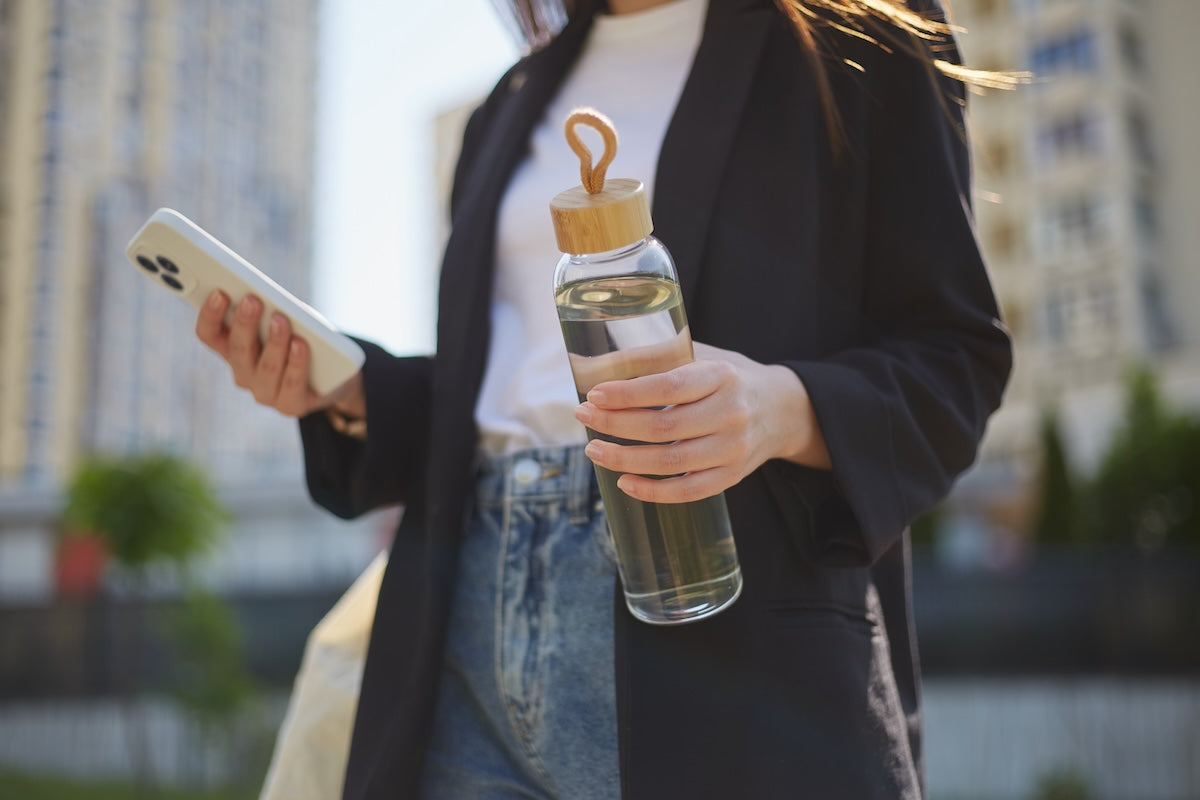 Young woman carrying a glass water bottle on the street.