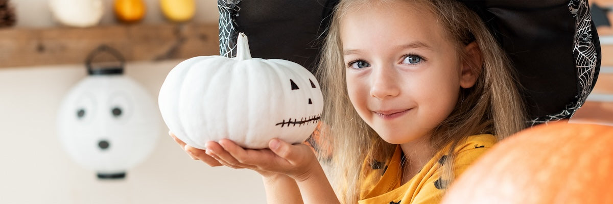 Young blonde girl holding a white pumpkin painted to look like a jack-o-lantern