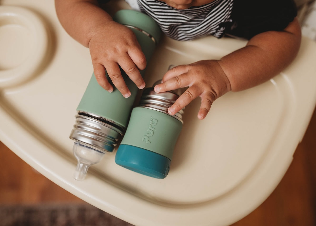 Ethically ambiguous baby boy playing with plastic-free baby bottles