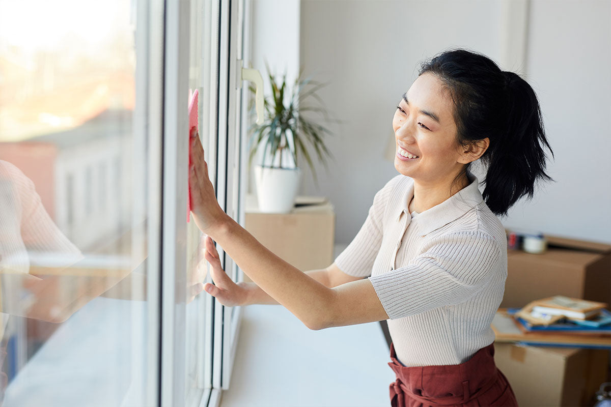 Young, attractive, smiling woman cleaning windows in her house.
