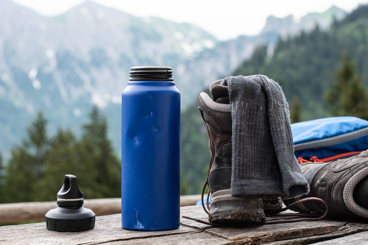 A damaged plastic and painted stainless steel water bottle in a park