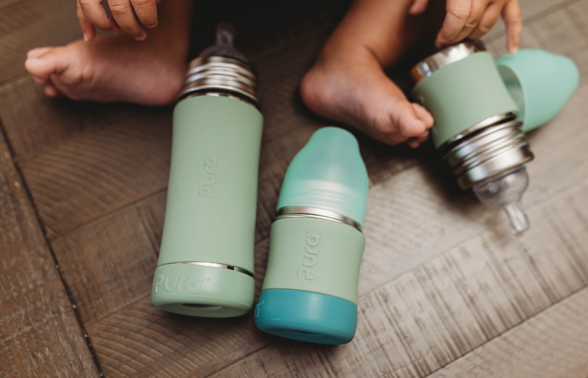 Ethnically ambiguous baby’s feet next to three stainless steel baby bottles